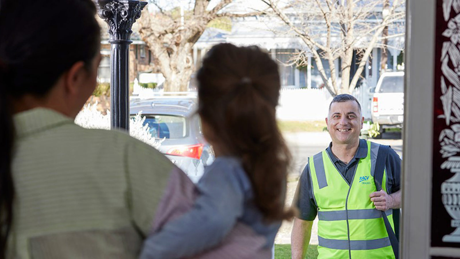 Woman holding a young child greets smiling tradesman at the front door.