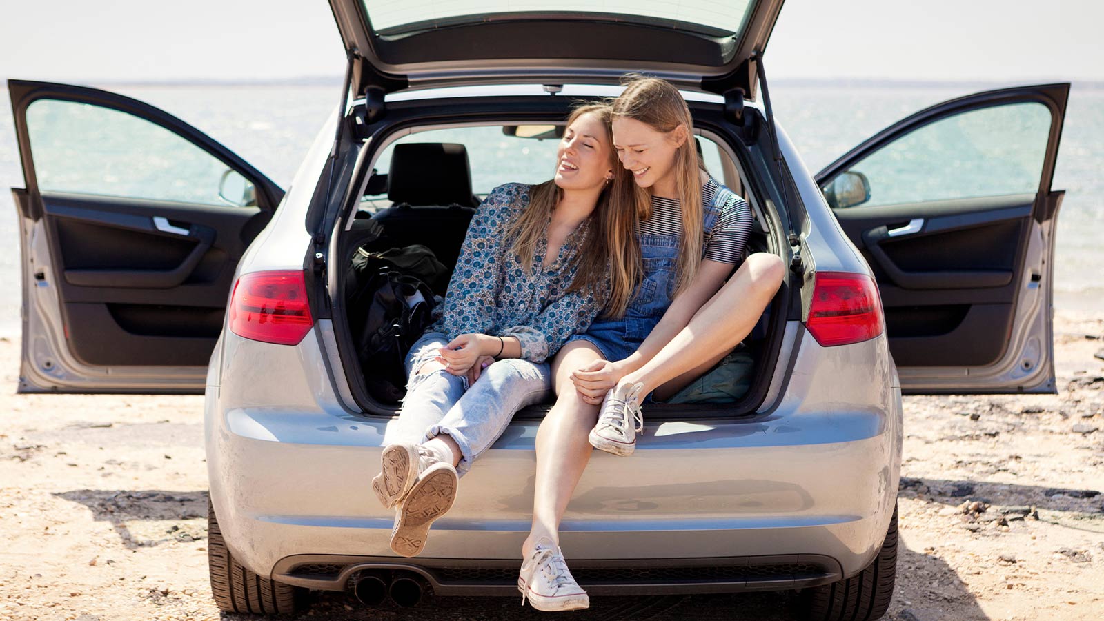 Two friends laughing and sitting in the boot of a car. 