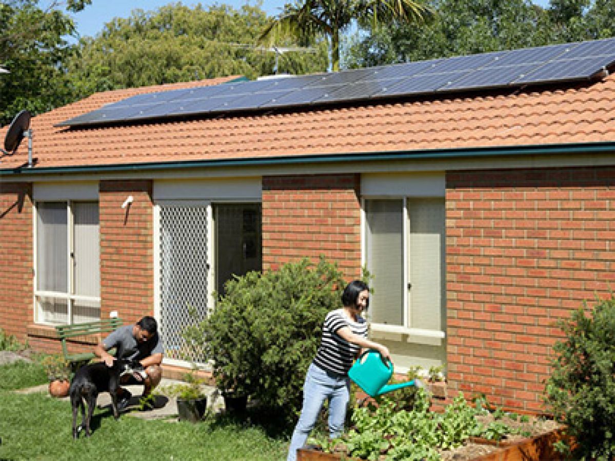 Couple outside of their Heidelberg family home fitted with Solar panels, watering the garden and playing with their dog. 