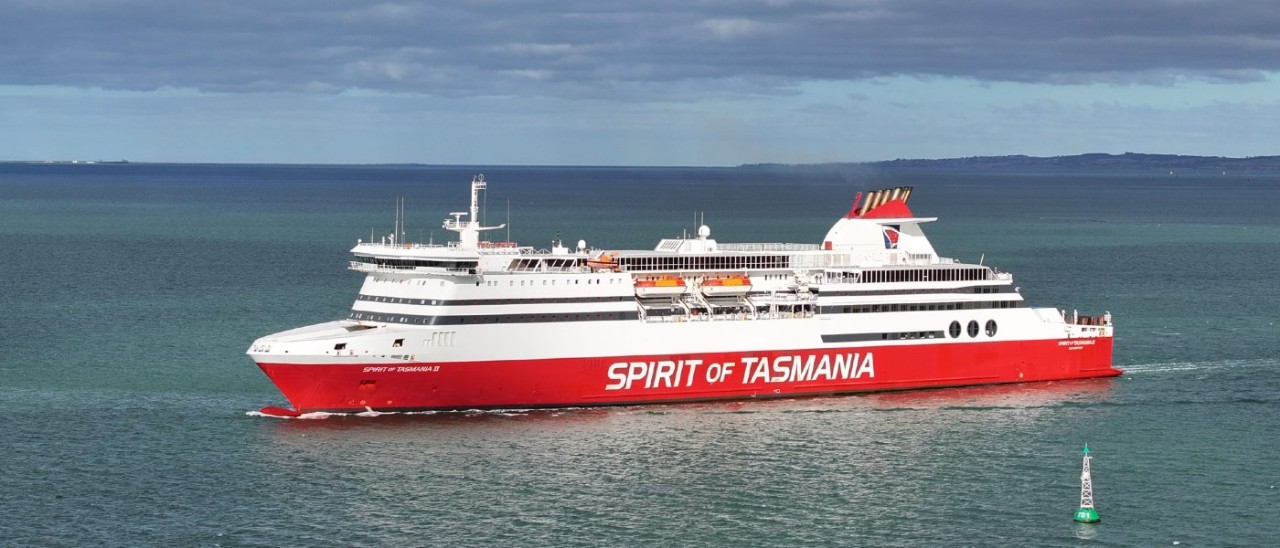 Spirit of Tasmania sailing on steely blue-green waters. A green buoy can be seen in the foreground while land can be seen in the distant background