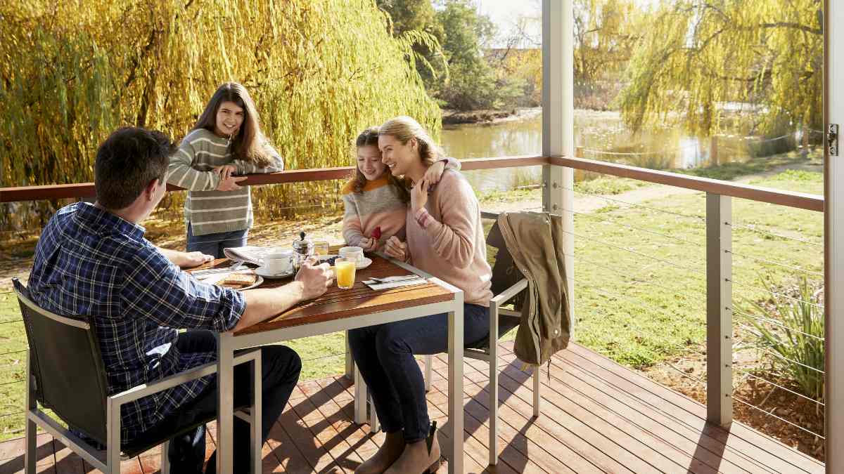 family having breakfast on cabin balcony near river