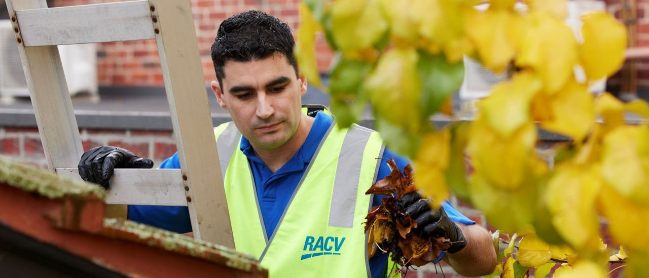 RACV worker on a ladder cleaning gutters