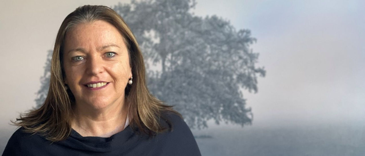 Close up of Kathryn Ryan with a painting of a tree in the background
