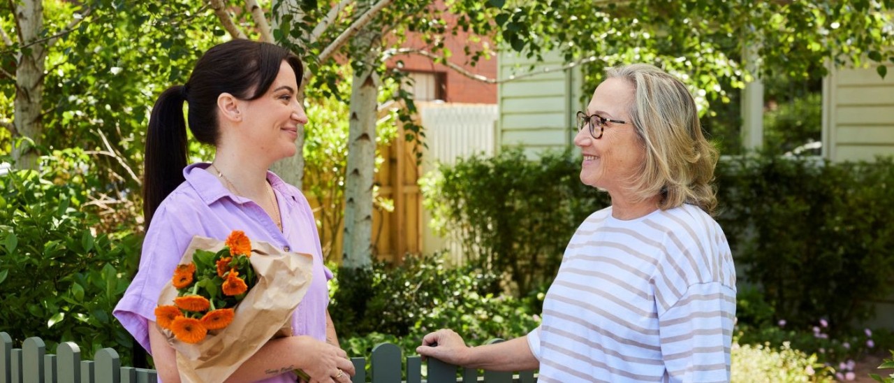 Two women standing outside next to a gate, one of the women is folding a bouquet of flowers