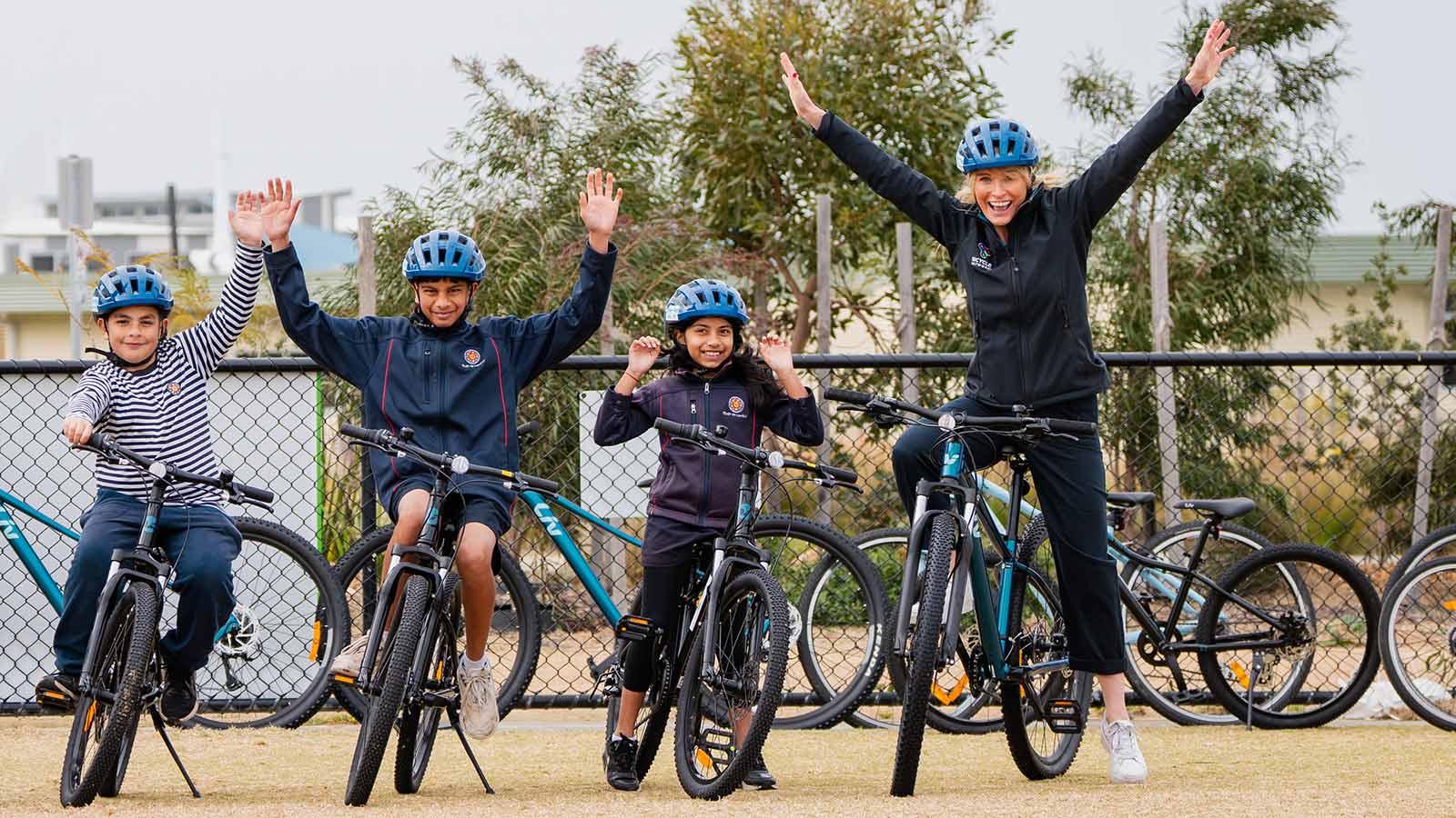 Woman and three children on bikes with blue helmets cheering.