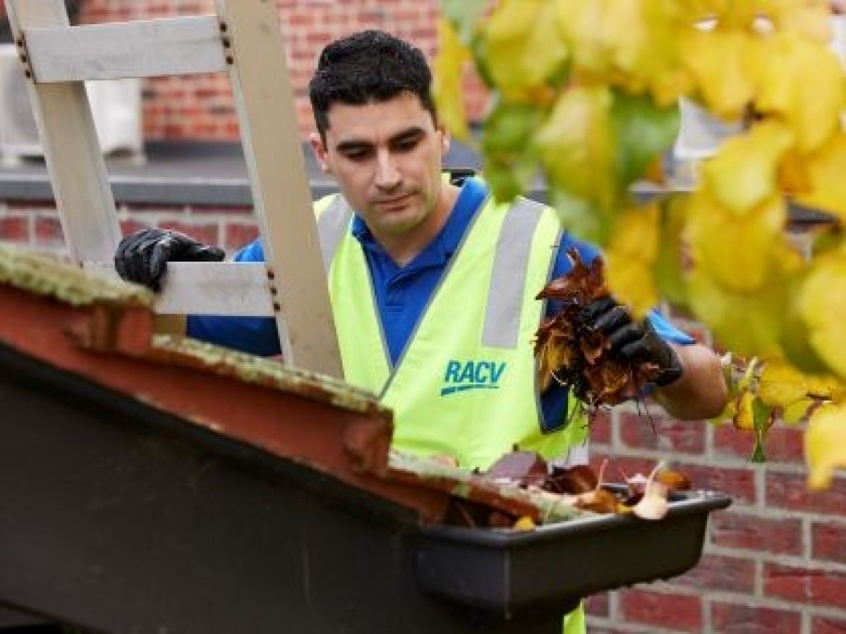 RACV worker on a ladder cleaning the gutters