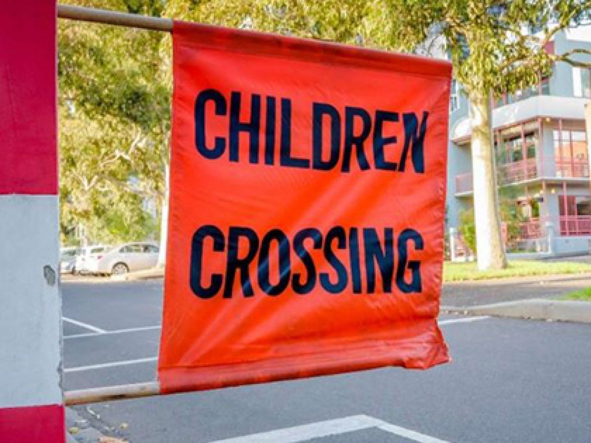 An orange flag with the words "children crossing" on it at a pedestrian crossing.