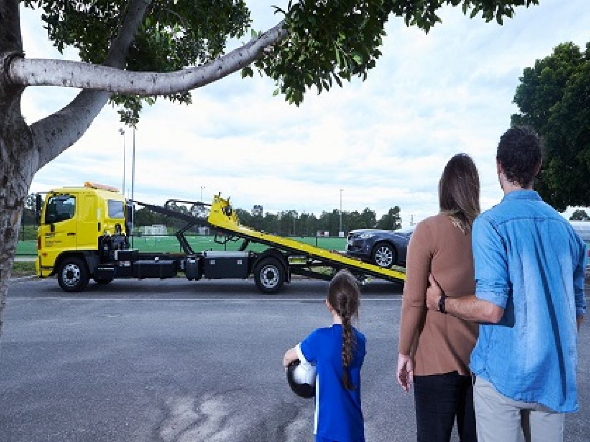 A man and a woman standing with a child watching a car being towed by RACV.