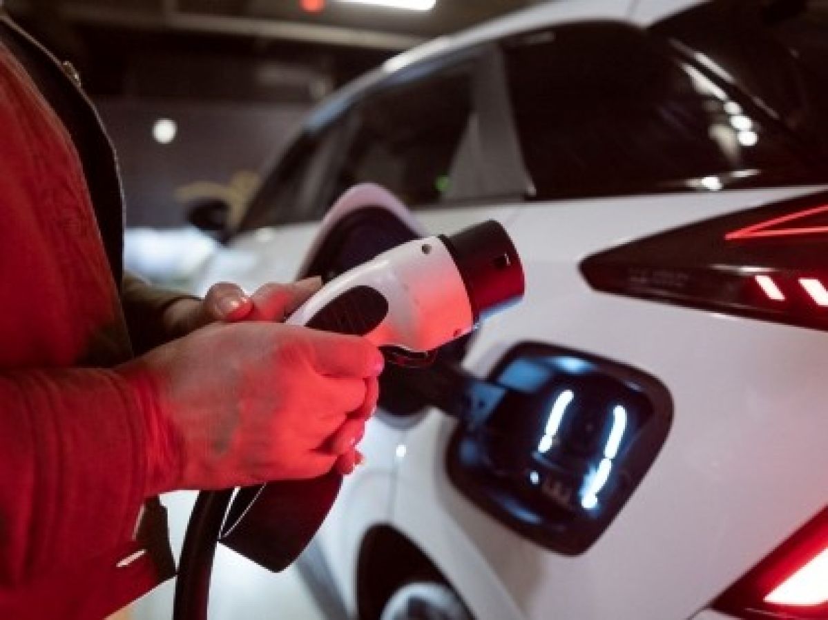 Person holding the plug of an EV charger, standing in front of their EV
