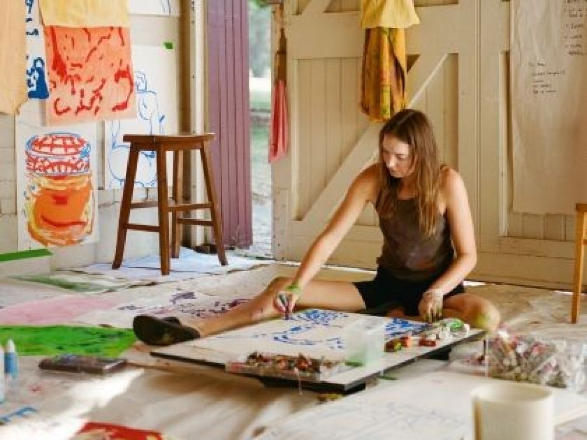 Artist Evie Cahir in her studio sitting on the ground painting an artwork