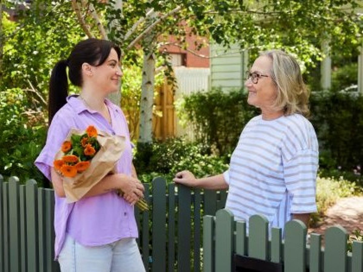Two women talking to each other outside a fence, with one woman holding flowers