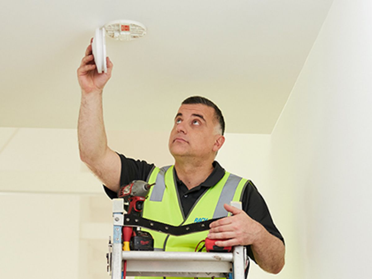Tradie installing a fire alarm on a ceiling.