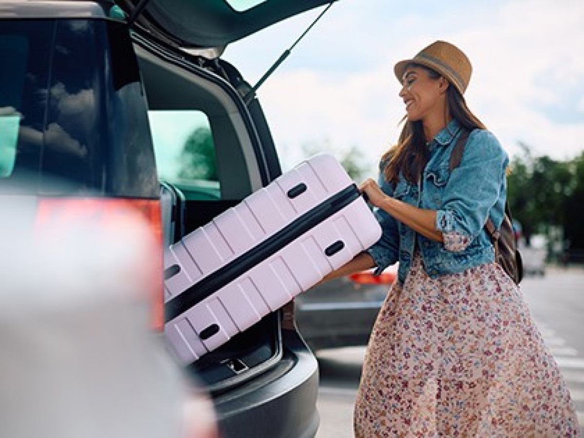 A woman lifting her pink suitcase from out of her car
