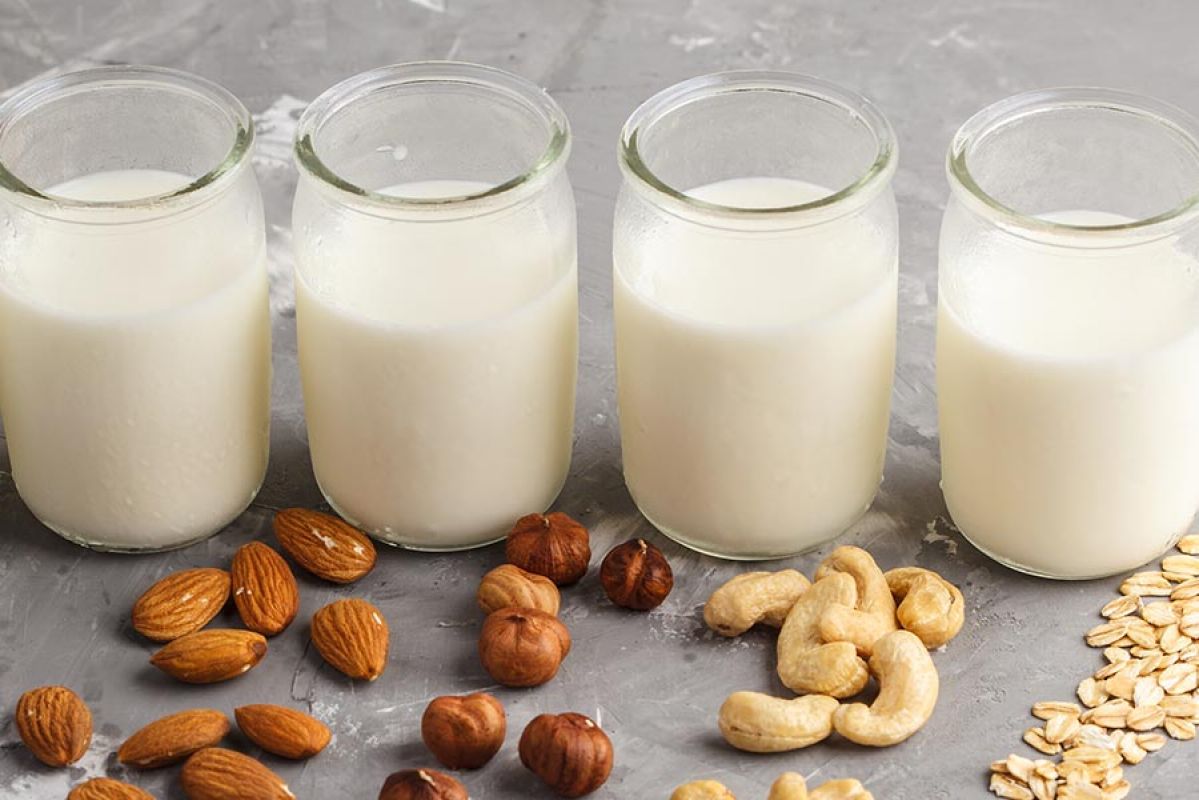 Close up of glass of oat milk with raw oats scattered around 