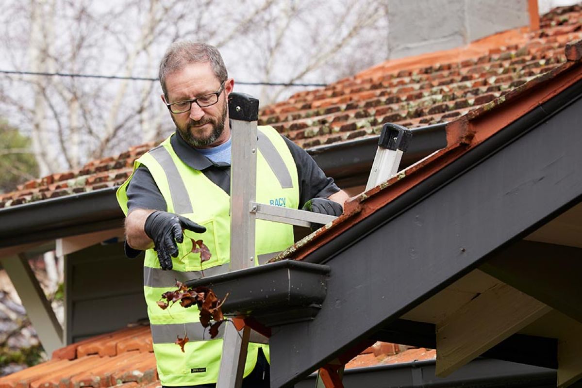 man on ladder removing leaves and debris from gutters on the roof