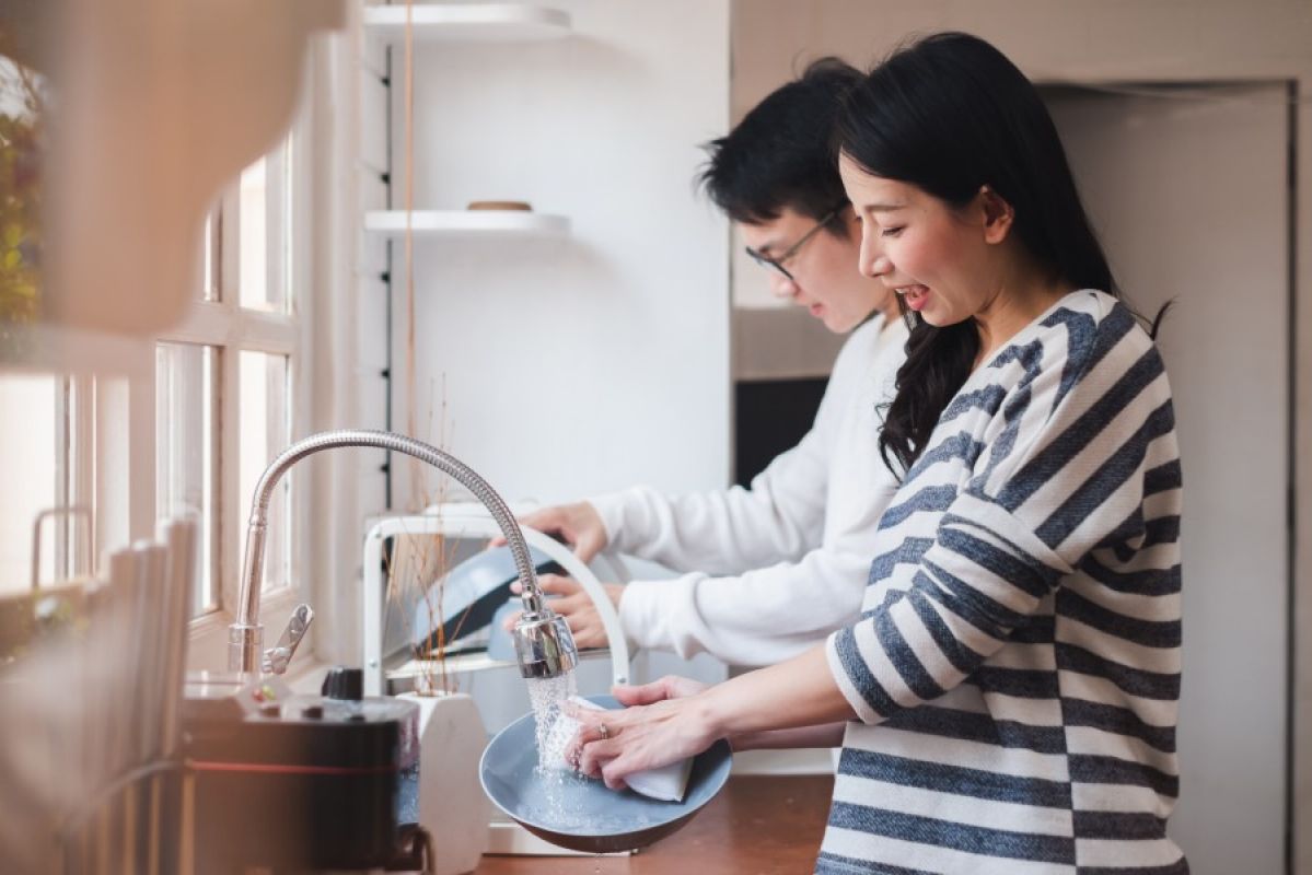 man and woman washing dishes together at kitchen sink