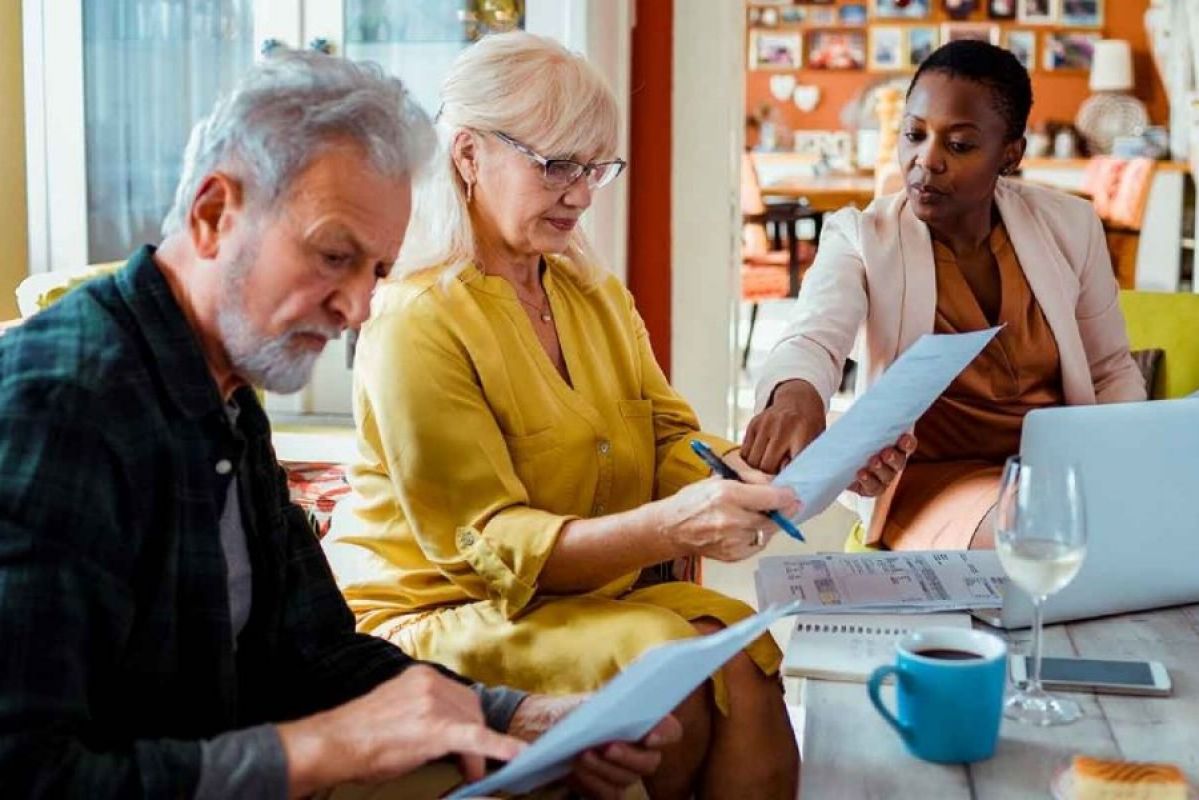 elderly couple sitting at table in home with real estate agent signing papers