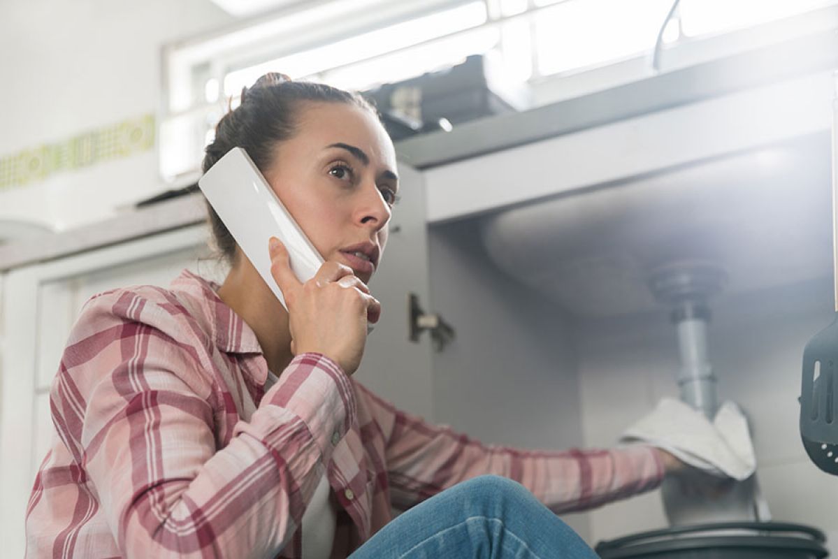 woman on the phone as she tries to fix leaking tap 