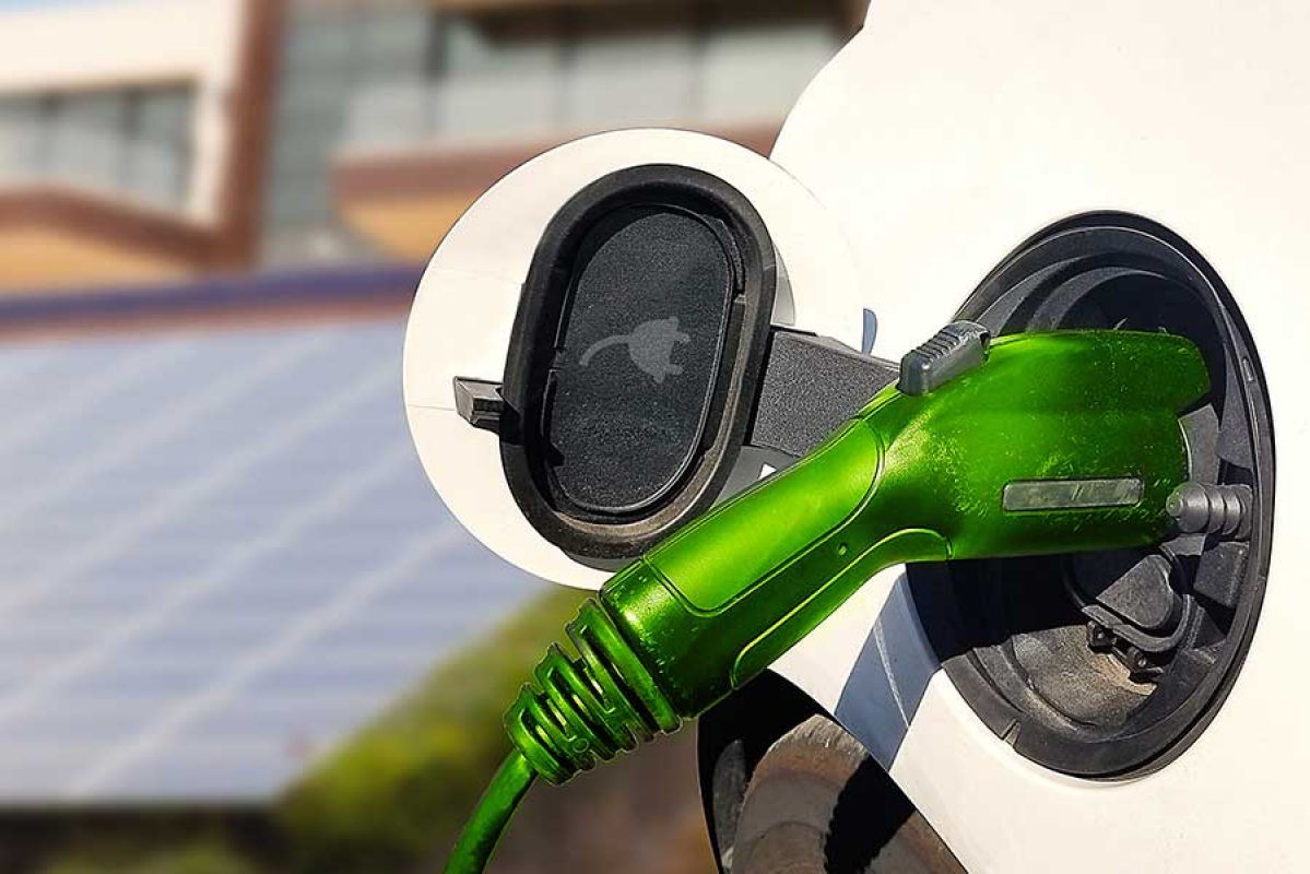 Electric vehicle charging pump with solar panels in background.