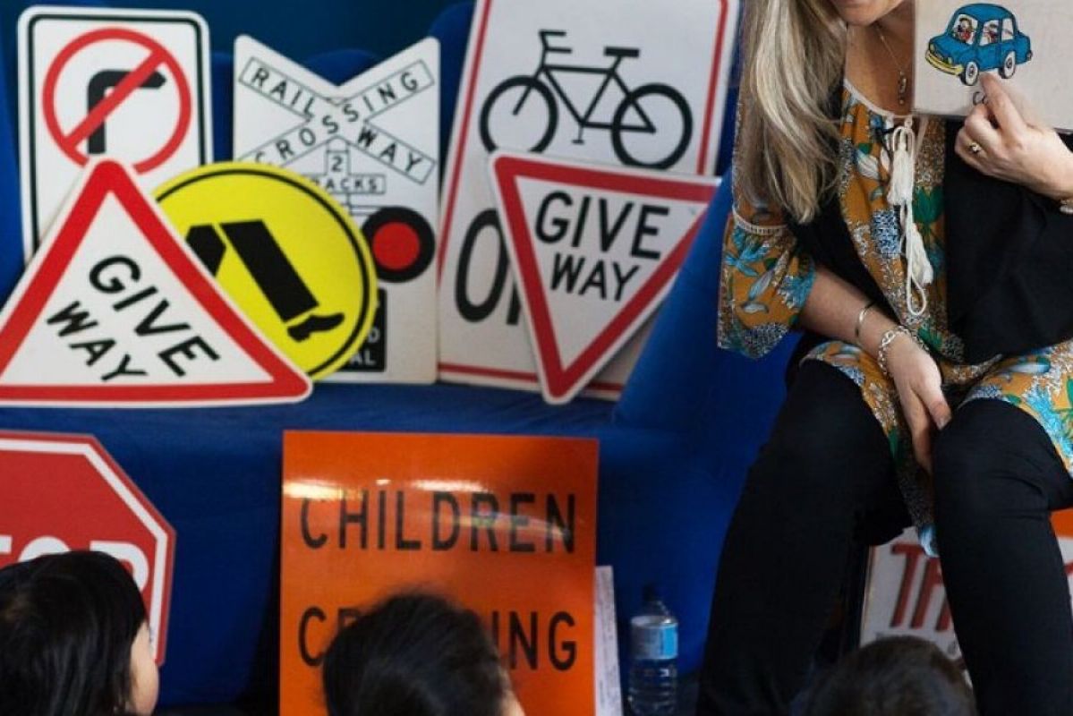 woman teaching seated children about safety with various road signs