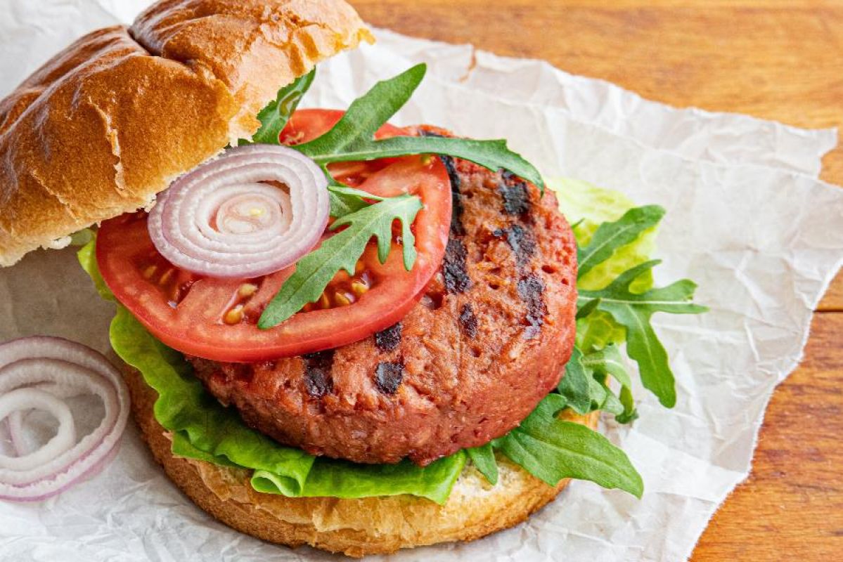 A plant-based burger with crisp lettuce, sliced tomato and onion on a golden bun