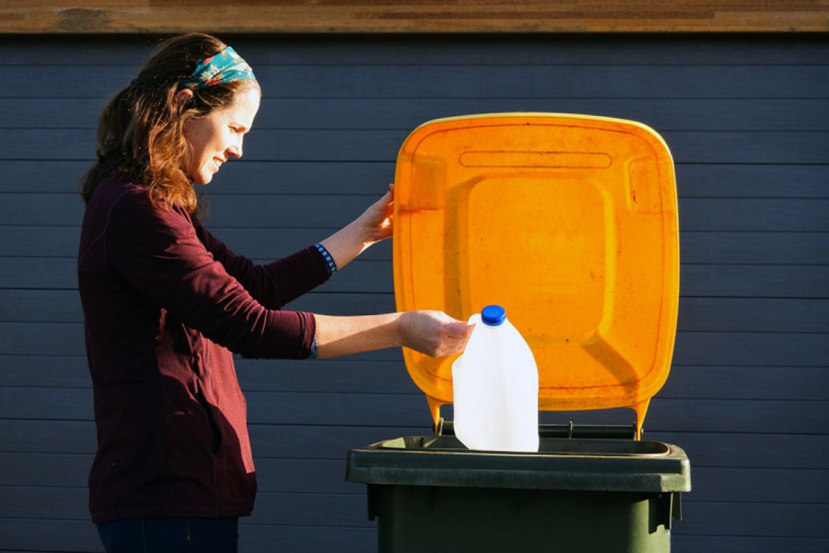 A person putting a milk bottle into a recycling bin