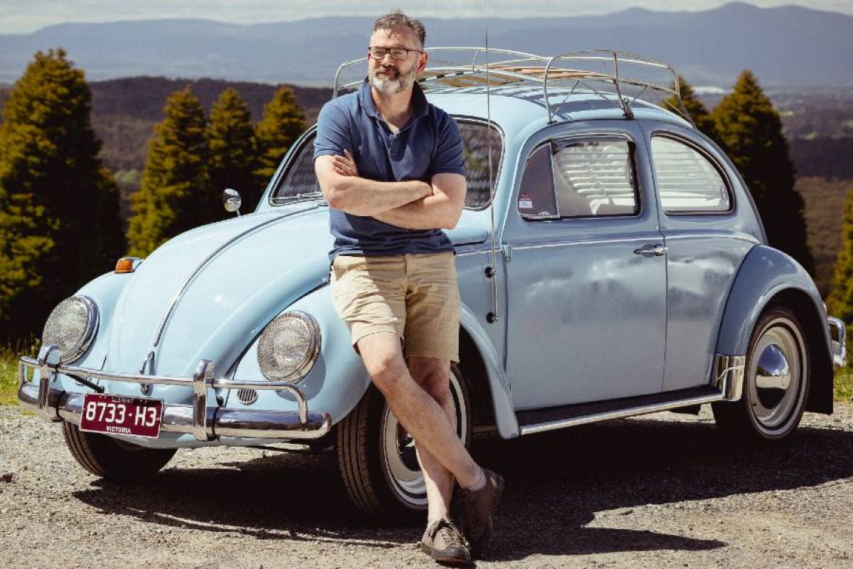 man standing in front of blue volkswagen beetle