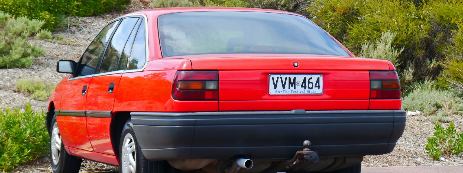 back of red toyota lexcen parked near shrubs