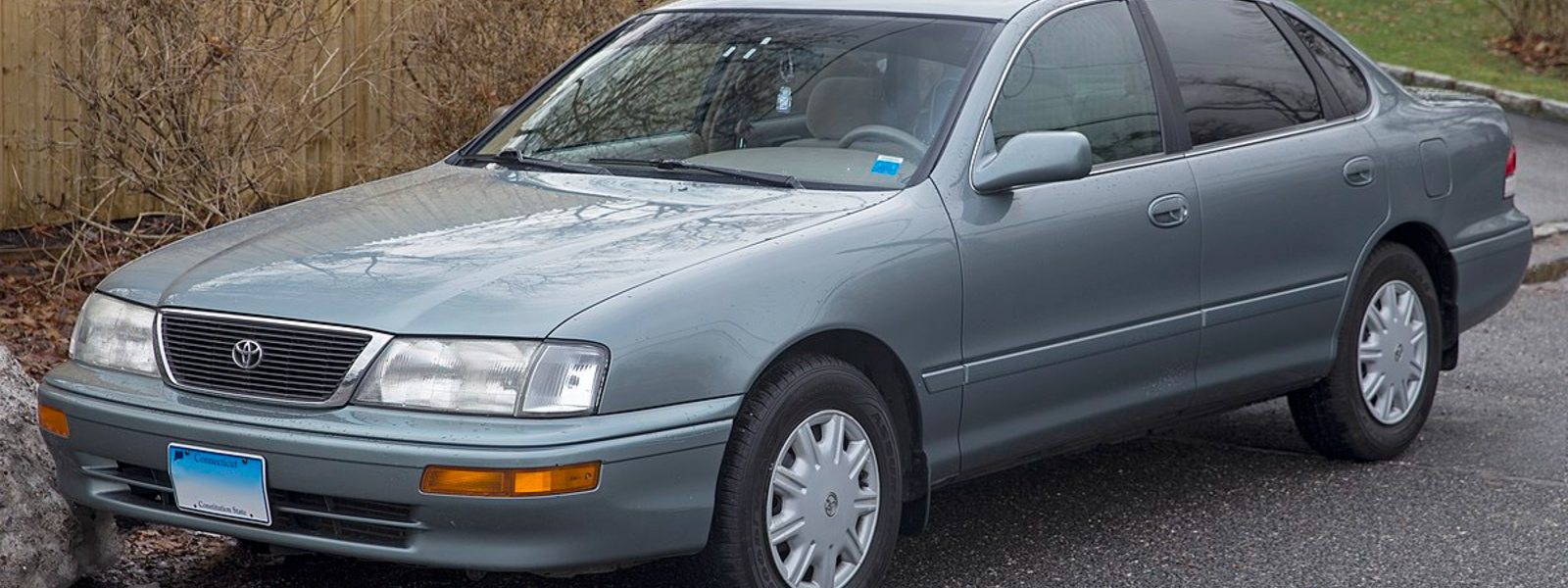 grey blue toyota avalon parked in front of wooden picket fence and grass