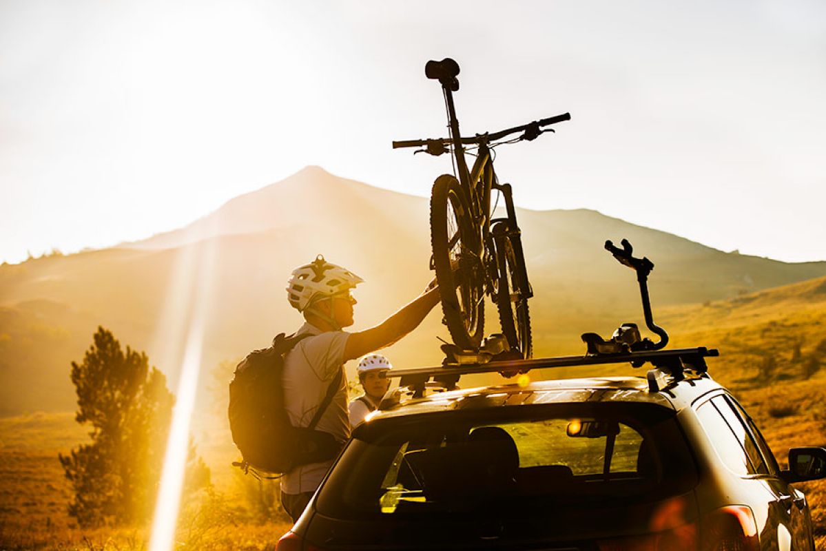 person securing bicycle on car roof rack