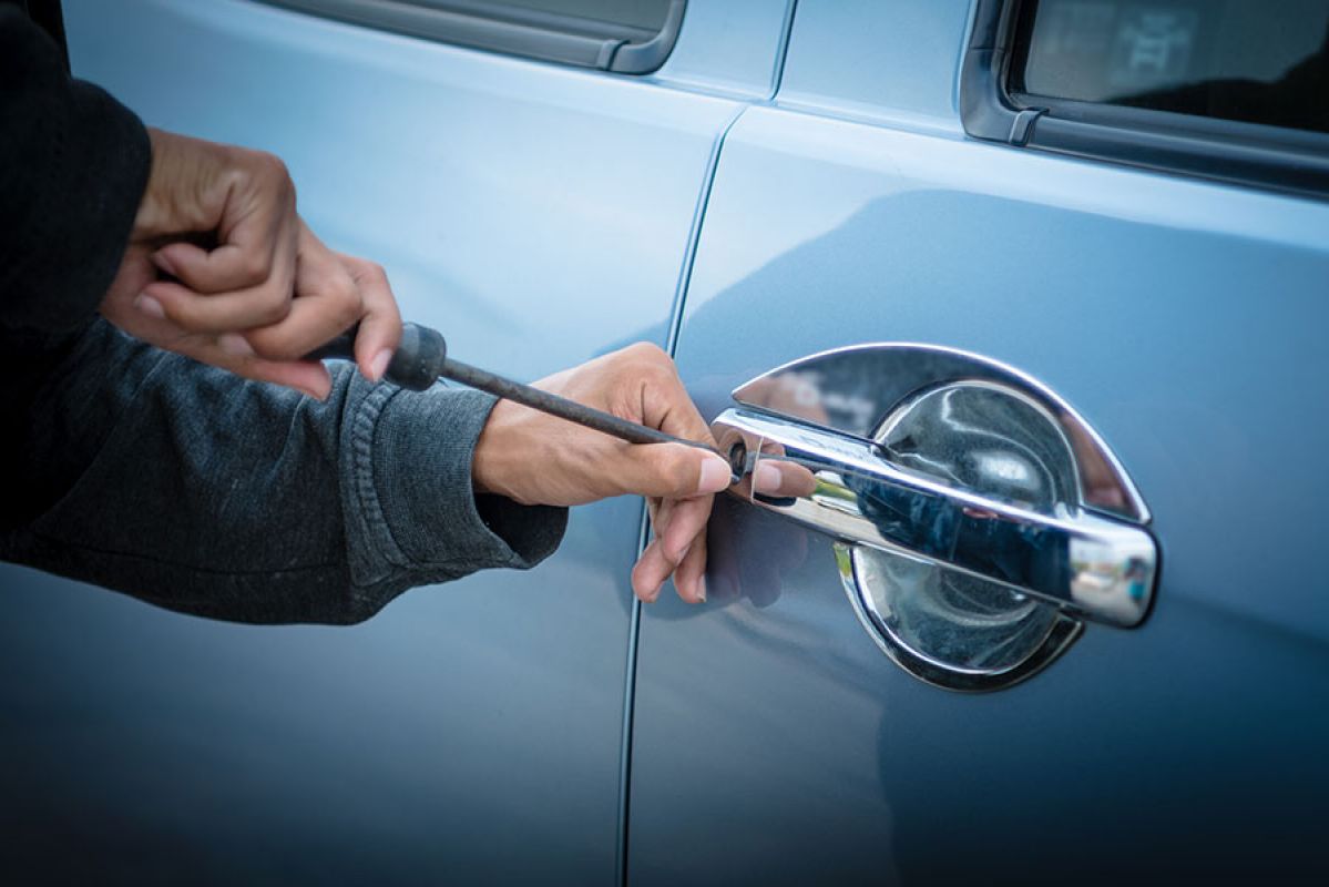 thief trying to break into a car with a screwdriver