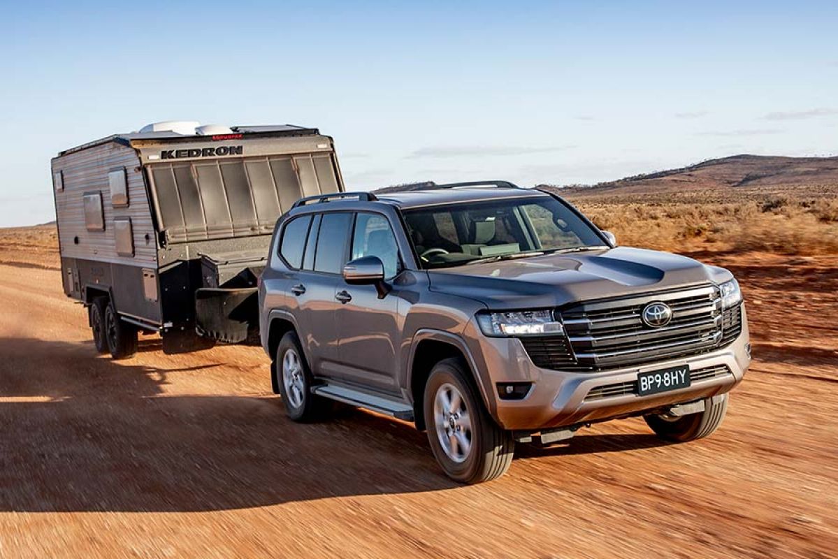 A car towing a caravan along dusty red dirt road in the outback