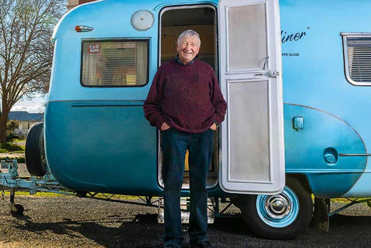 Smiling man stands in front of his blue caravan.