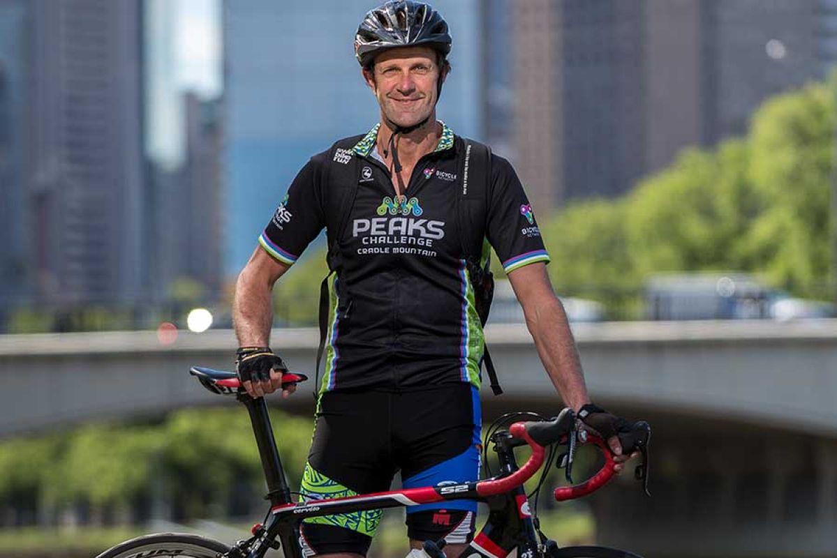 Commuter standing with his bike with city in background.