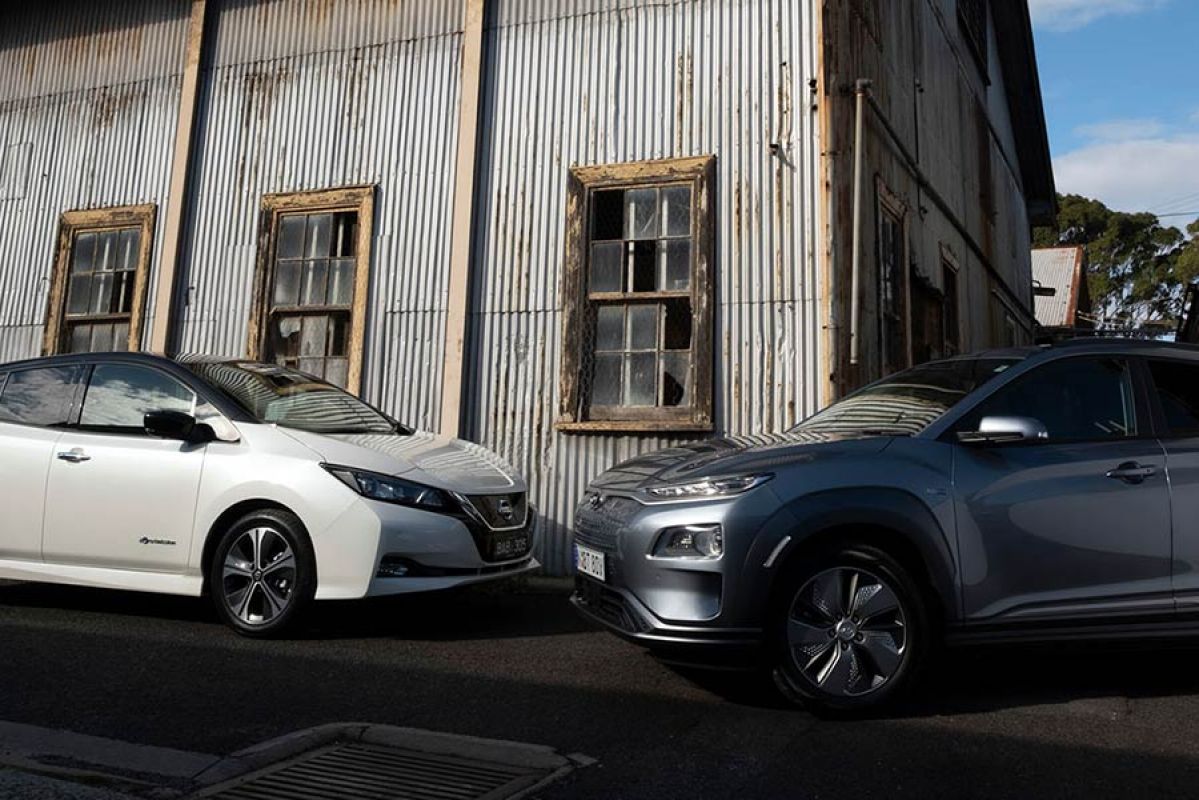 Side view of a white Nissan Leaf parked next to a dark grey Hyundai Kona Electric Highlander