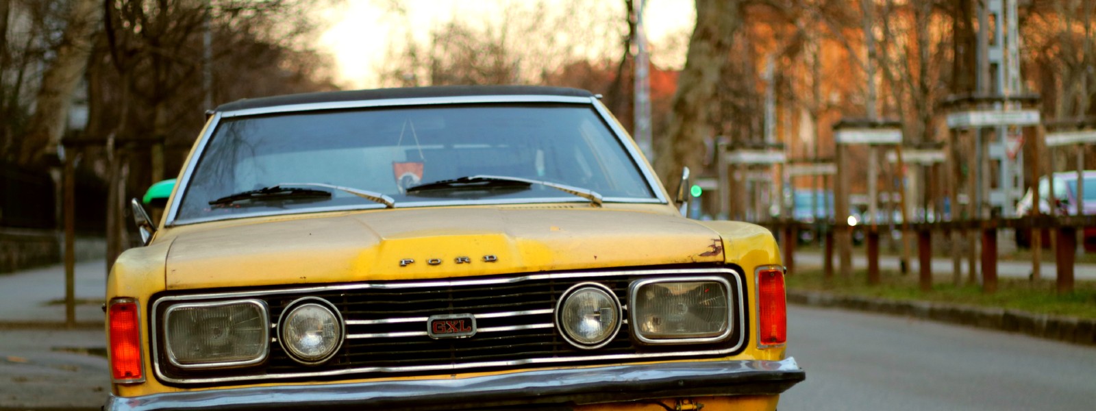 yellow ford cortina parked on street next to trees and sidewalk