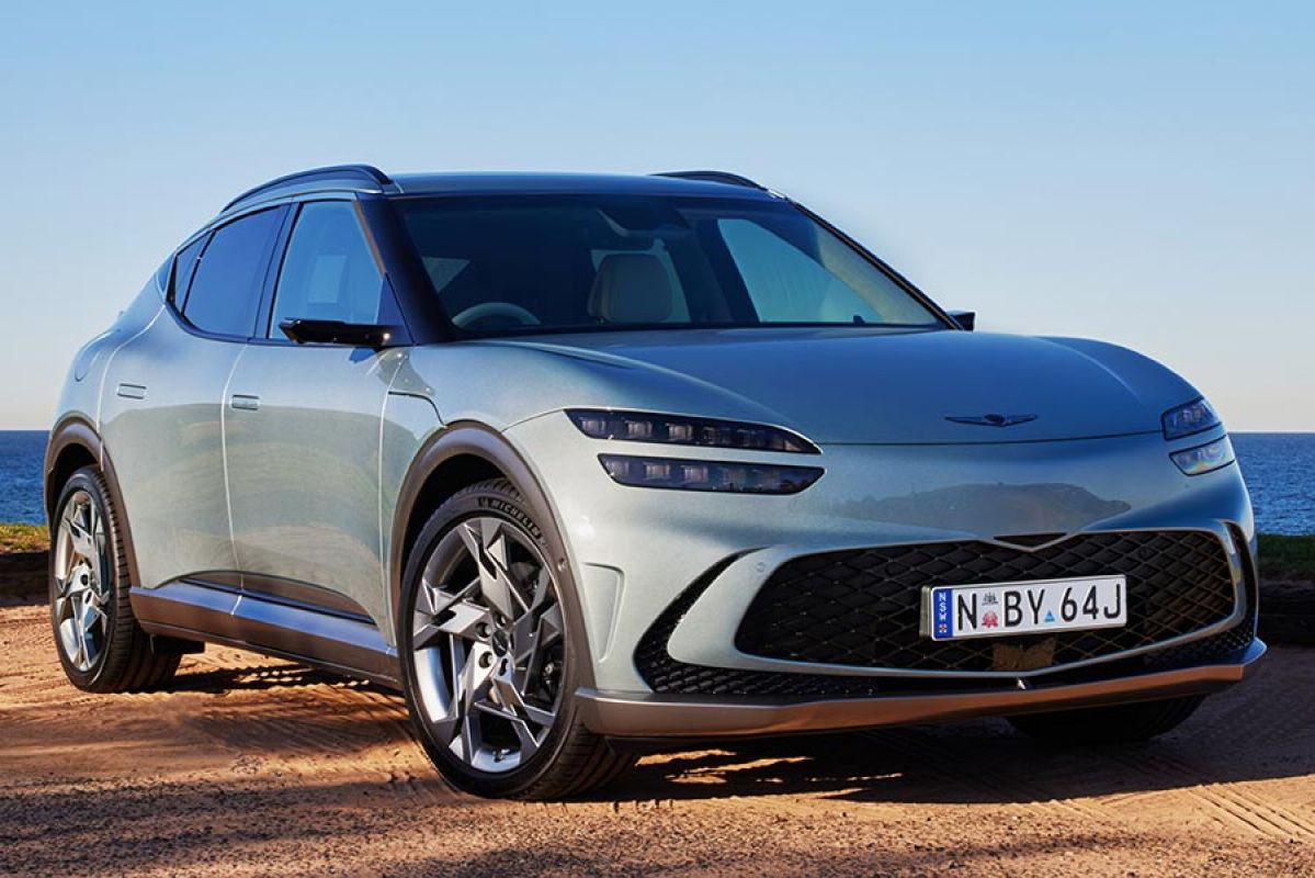 A blue Genesis GV60 is parked on a cliff overlooking the sea.