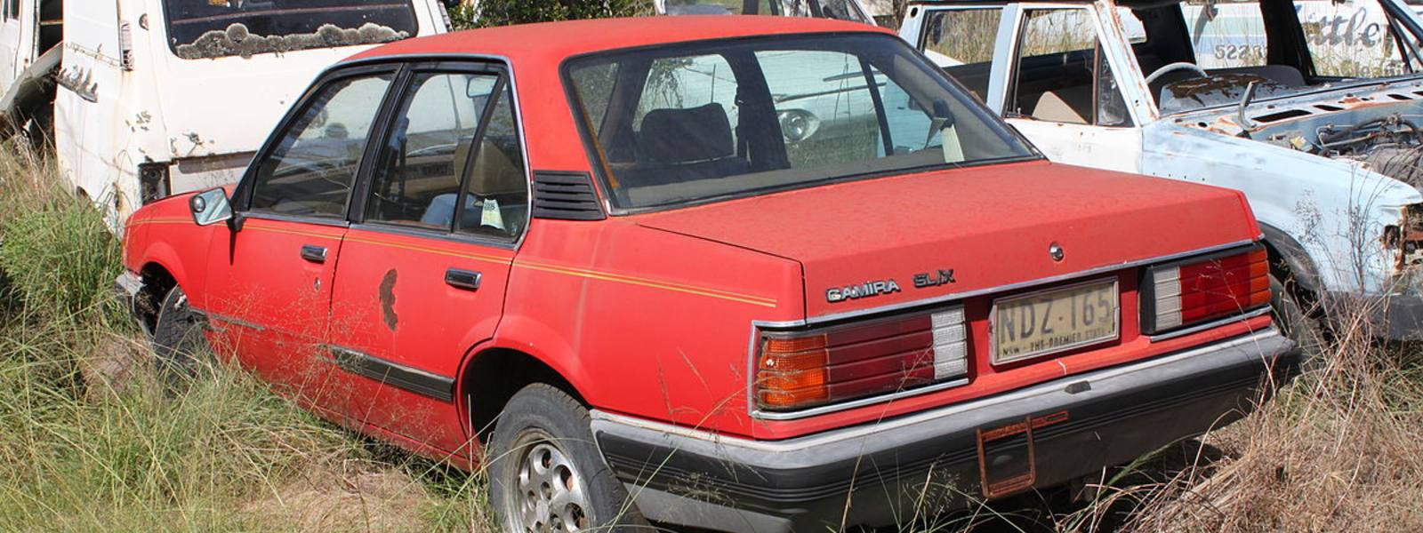 old red holden camira parked in weeds and bushes