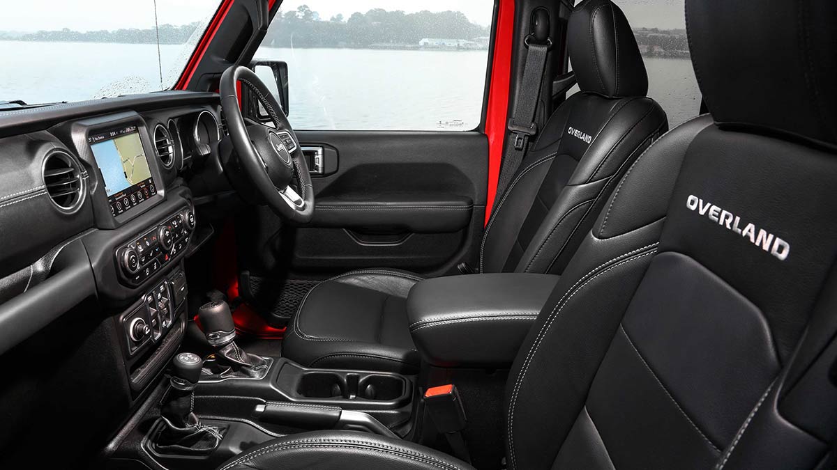 The dark grey and black interior of the Jeep Wrangler JL 2019 showing the front seats, dashboard and steering wheel
