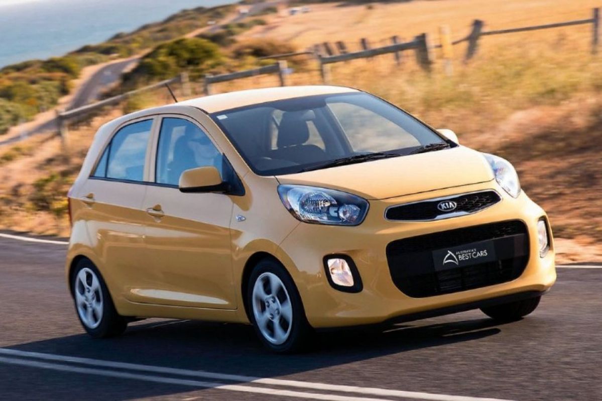 yellow kia picanto s driving on great ocean road with shrubs in background