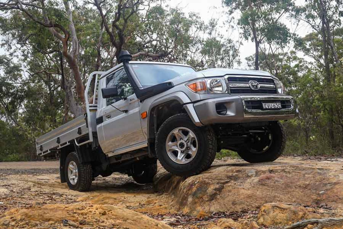 A silver toyota landcruiser 70 series parked on top of a small rocky mound in the bush