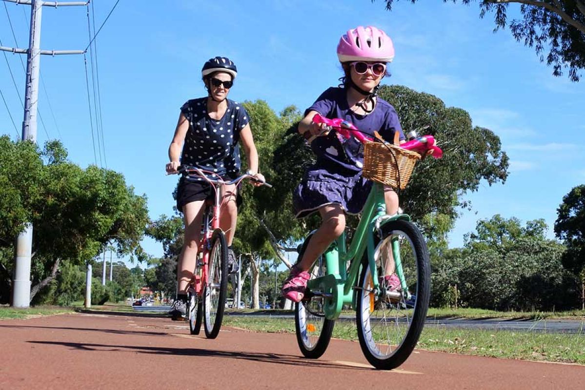 A woman and child wearing helmets as they cycle along a bike path