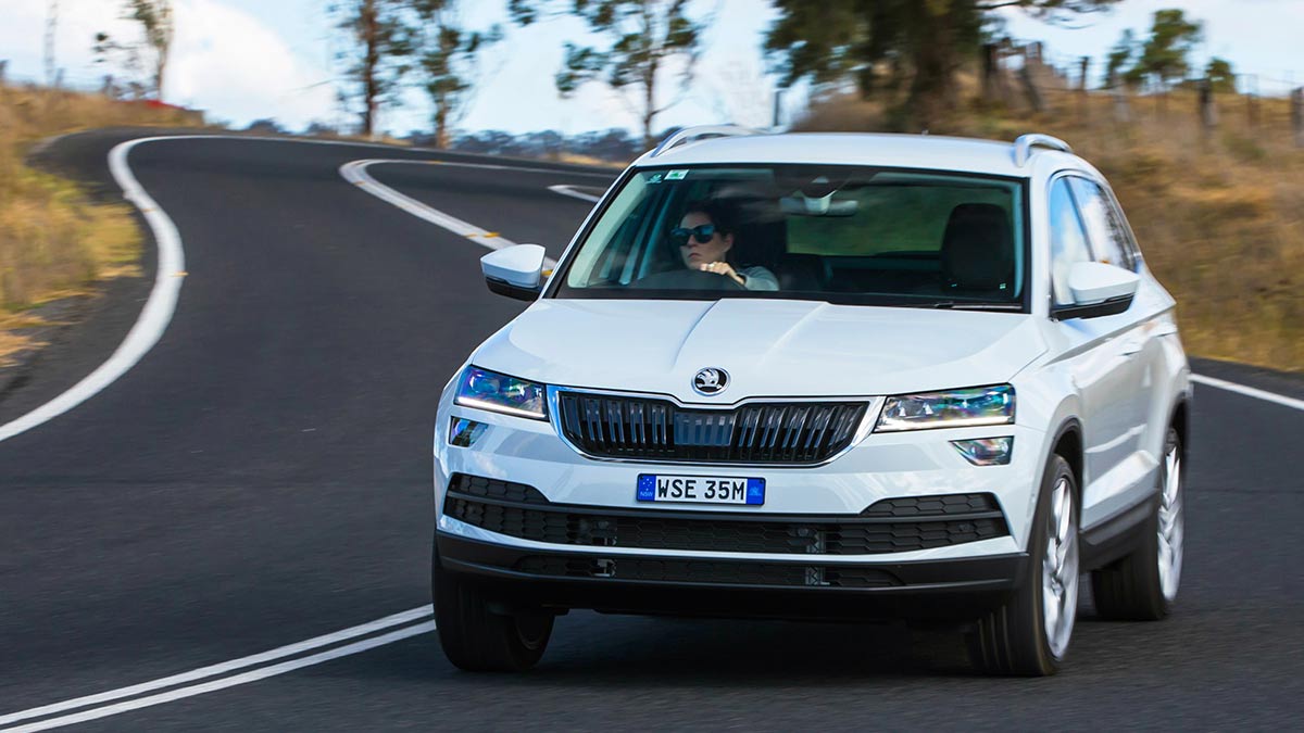 Front view of a white Skoda Karoq 2019 car driving down a winding country road