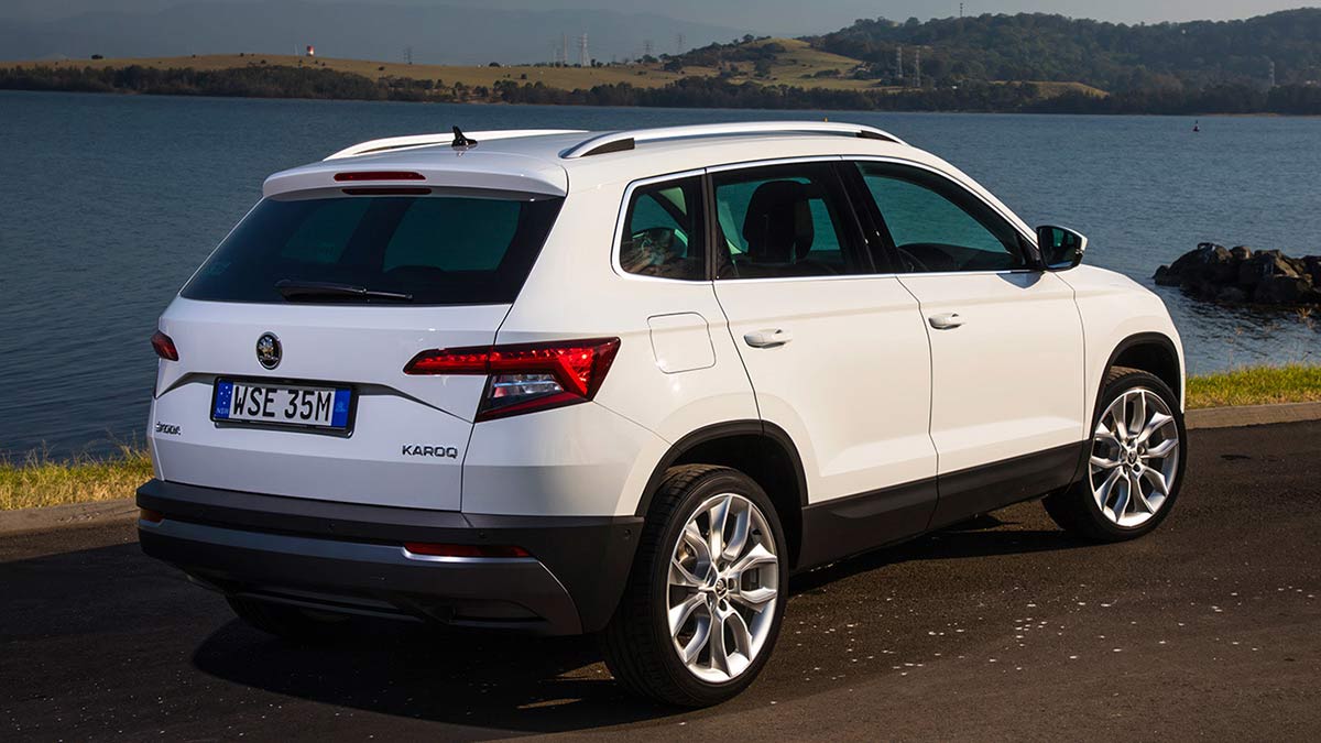 Rear side view of a white Skoda Karoq 2019 car parked next to a lake