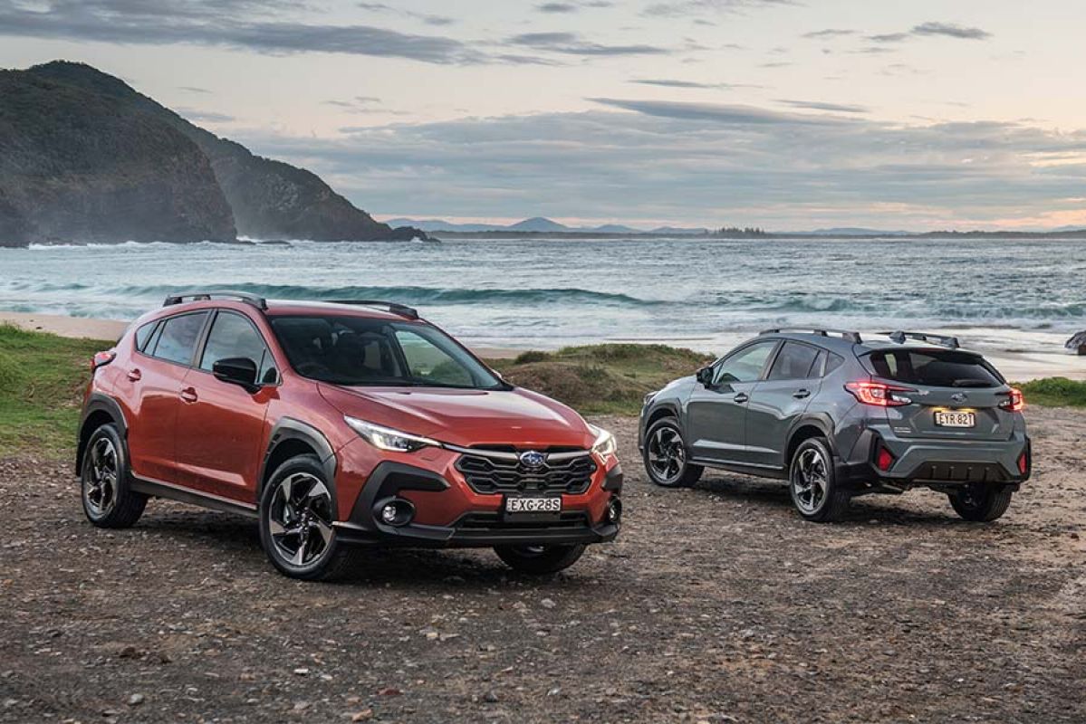 A grey and an orange Subaru Crosstrek parked on a rocky beach 