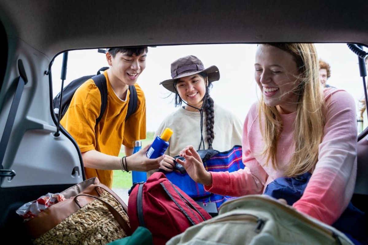 three young adults taking sunscreen from the boot of their car