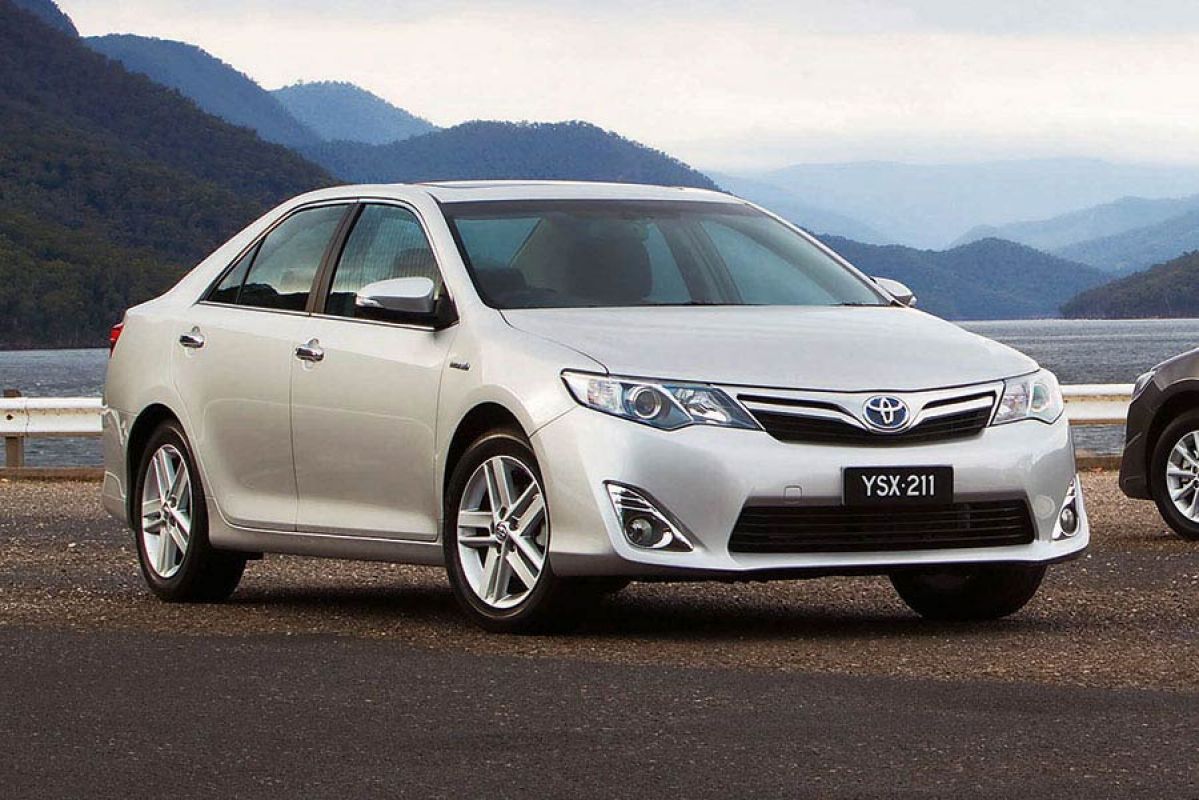 grey totyota camry parked on road in front of lake and mountains