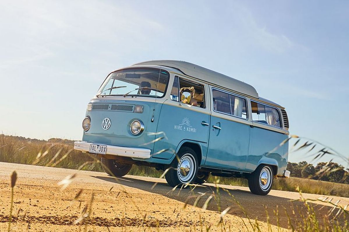 blue kombi van driving on a road next to a field
