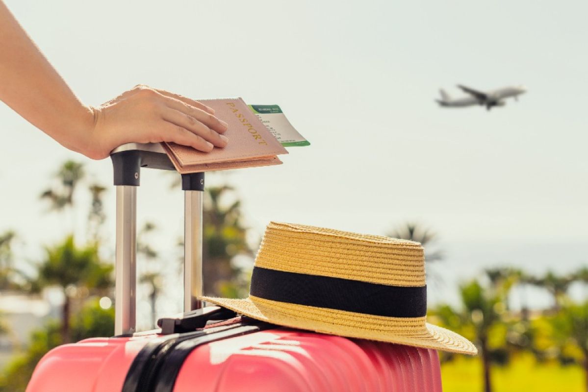 woman holding passport and plane ticket looking at plane in sky