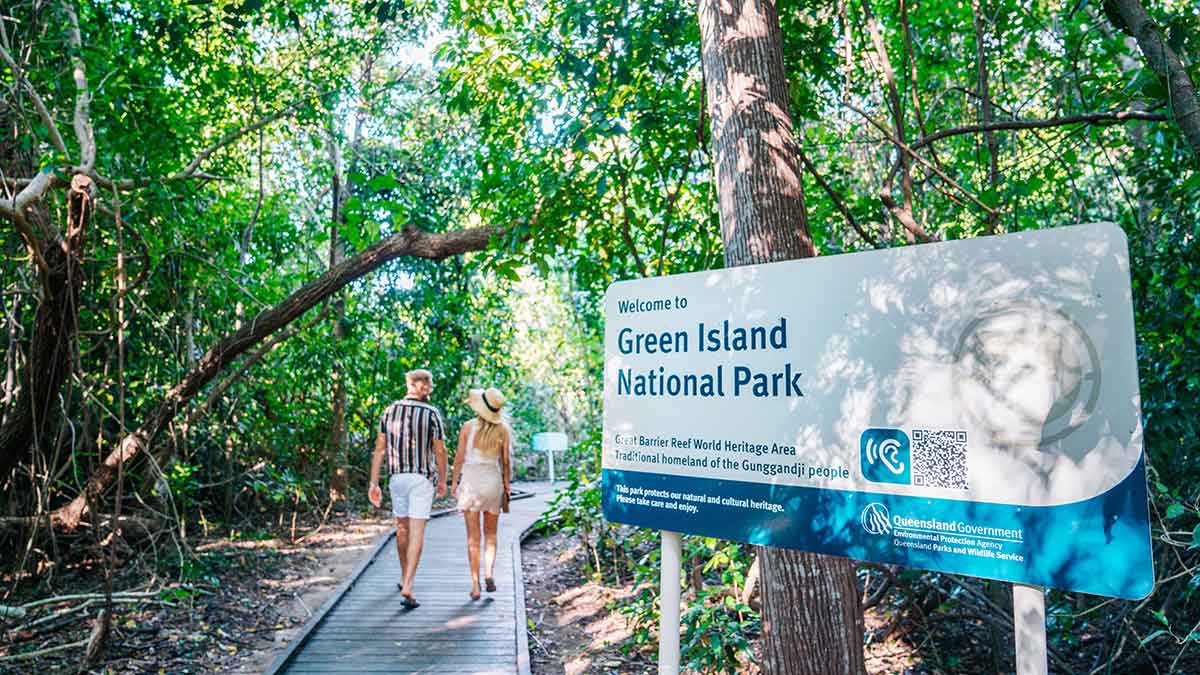 Two people walking on a boardwalk under leafy green trees
